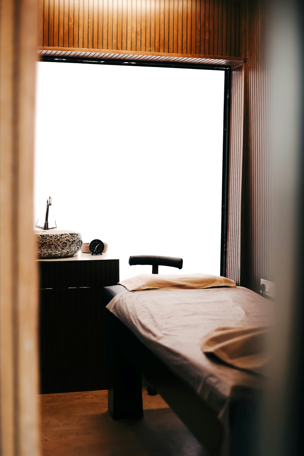 A calm treatment room with a linen-covered table beside a window of soft daylight